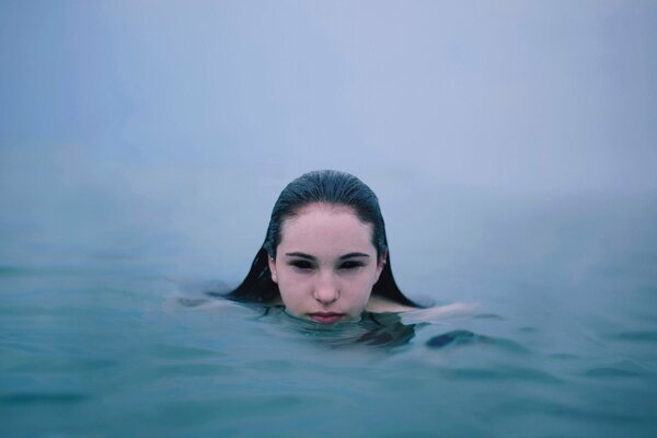 Das Mädchen schwimmt auf einem nebligen Fluss, nur der Kopf ist aus dem Wasser sichtbar