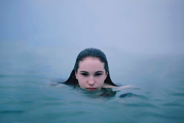 Девушка плывет по туманной реке, из воды видна только голова