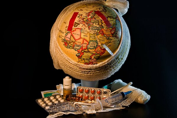 The globe of the world tied with a bandage with a thermometer and medicines