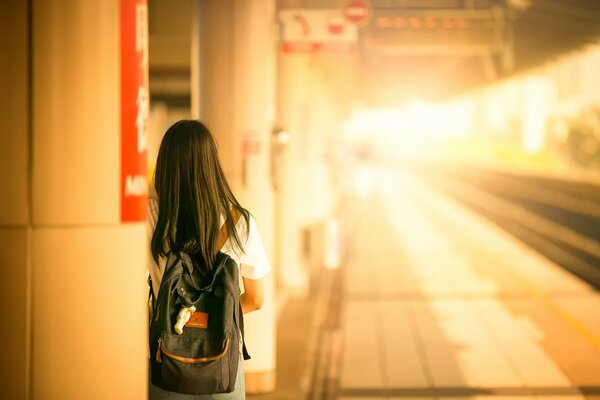 Dziewczyna z plecakiem stoi na dworcu i czeka na pociąg