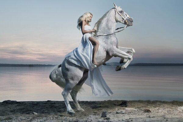 A girl in a white dress is sitting on a white horse. On the background of the lake