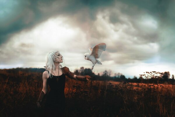 A woman with a white owl against a cloudy sky