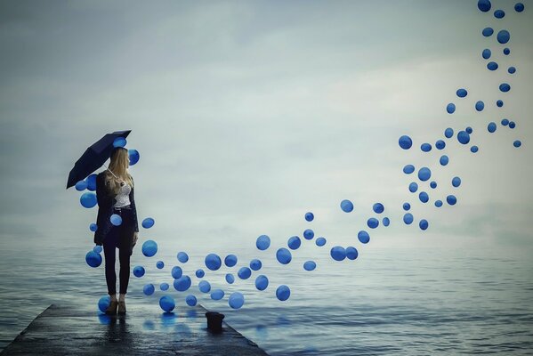 A girl with an umbrella looks after the flying balls in the sky