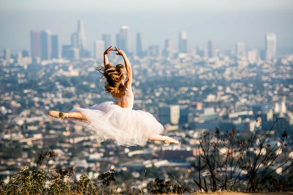 Девушка в белом платье танцует на фоне города
