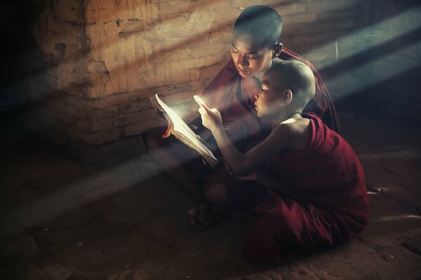 Les moines-les enfants sont assis et lisent un livre