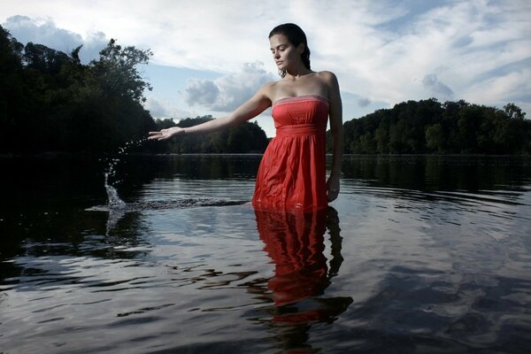 Ciemnowłosa dziewczyna w czerwonej sukience stoi po kolana w wodzie