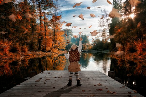 A girl on a bridge by the river plays with autumn leaves