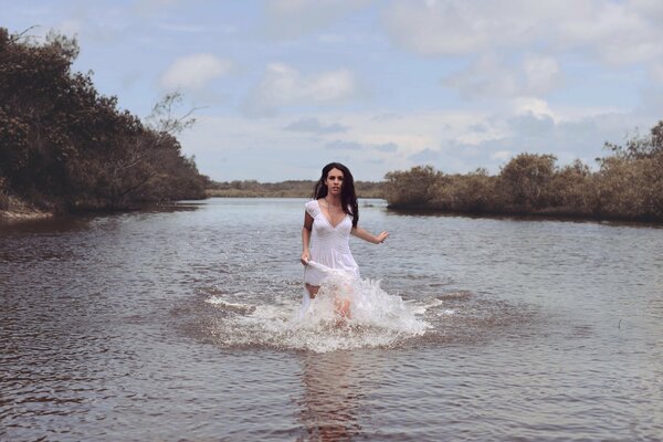 A girl in a white dress creates splashes in the river