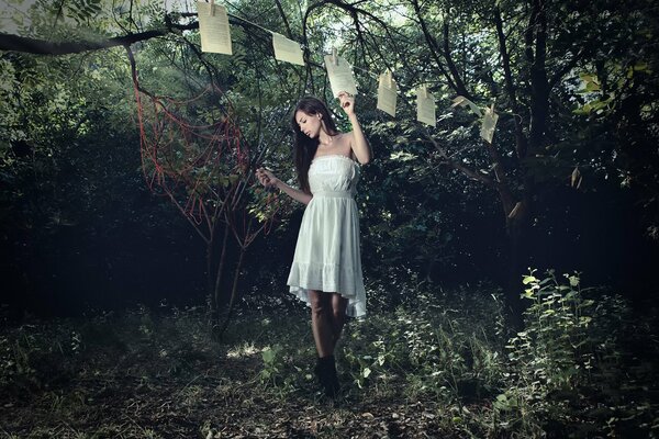 Una chica con un vestido blanco se aferra a una cuerda con pinzas para la ropa las hojas del libro, todo sucede en el bosque