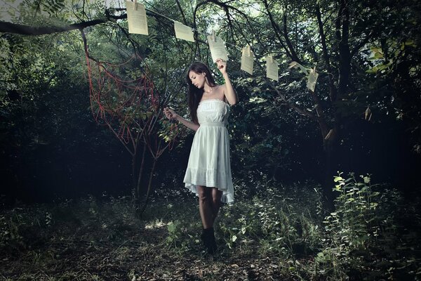 Dziewczyna w białej sukience przywiązuje się do liny z spinaczami do Bielizny arkusze książki, wszystko dzieje się w lesie