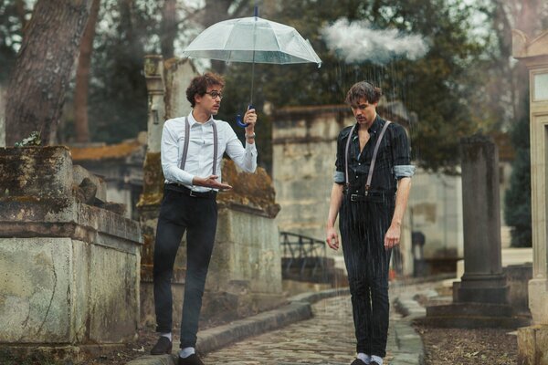 Two men in the rain, one of them under an umbrella