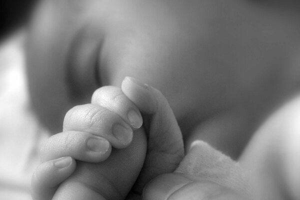 A sleeping baby holds an adult by the finger