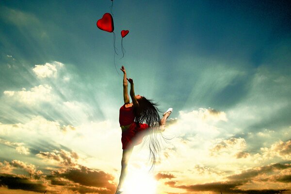 A ballerina girl holds heart balloons against the background of a sunset with clouds