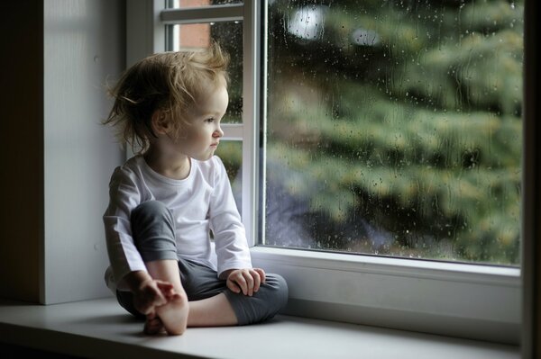 Kind, das im Regen aus dem Fenster schaut