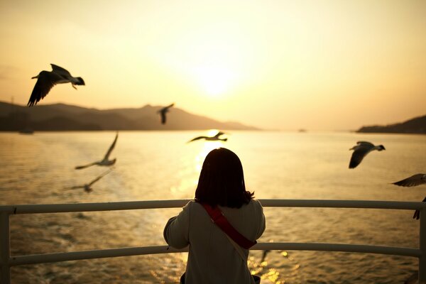 A girl watches the sunset on the stern of a boat