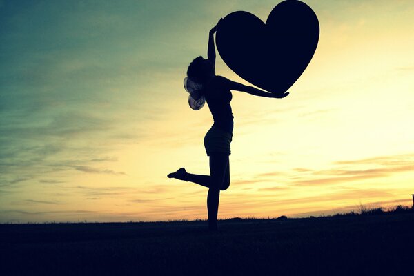 Foto de una chica alada al atardecer con un corazón