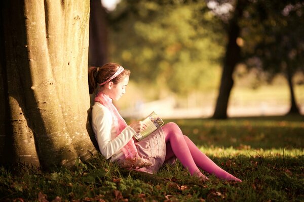 Dziewczyna siedzi pod drzewem i czyta książkę