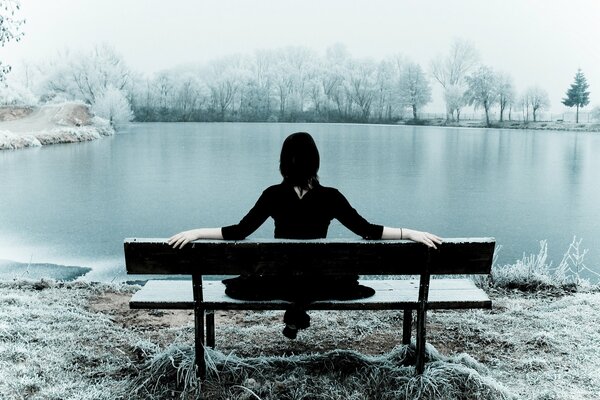 The girl is sitting on a bench by the lake