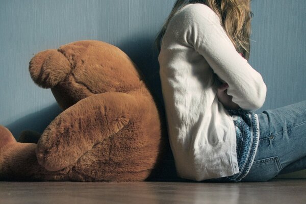 The girl is sitting with her back to the teddy bear