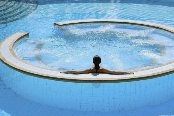 The girl is sitting with her back in the jacuzzi