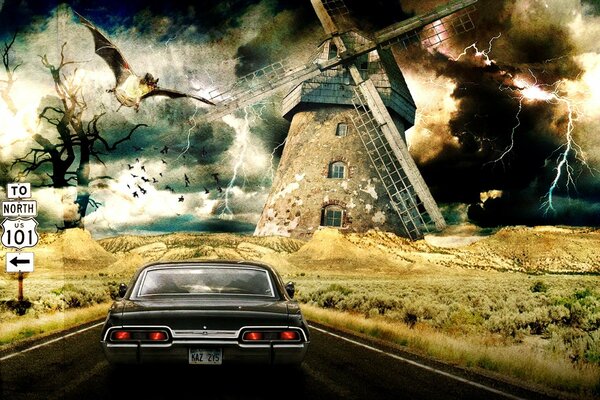 The car is driving along the road , to a distant mill with a bat