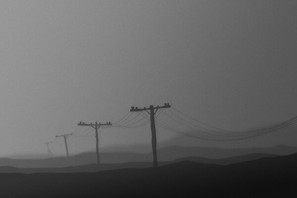 Postes con cables en la niebla nocturna. Gris y oscuridad