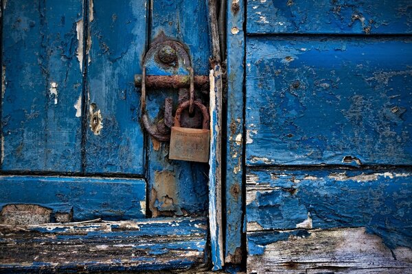 The lock is hanging on a blue door with peeling paint