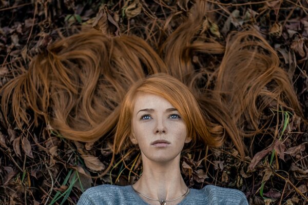 Porträt eines Mädchens mit roten Haaren auf dem Hintergrund der gefallenen Blätter