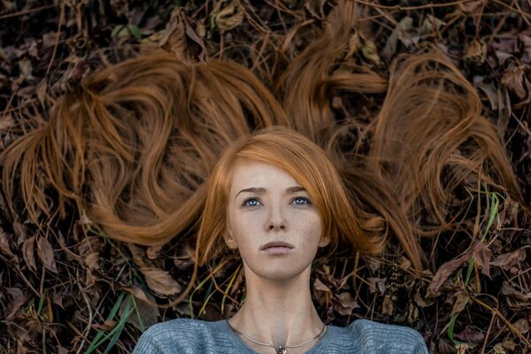 Portret dziewczyny z rudymi włosami na tle opadłych liści
