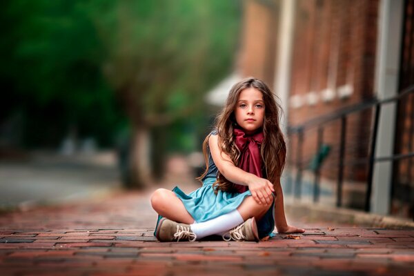 A girl in a dress and with a bow on her neck is sitting