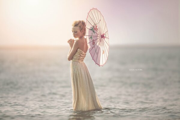 A girl stands in the sea with an umbrella