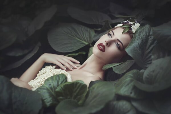 A girl in a pearl swimsuit surrounded by green leaves