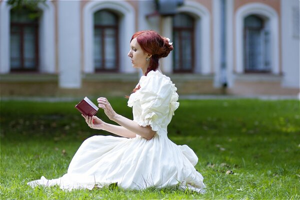Dziewczyna w białej sukience na trawniku czyta książkę
