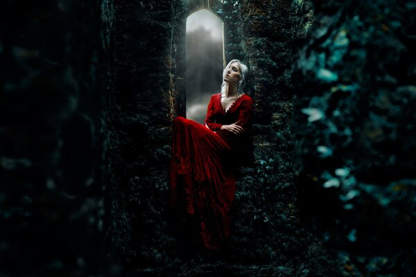 A girl in a red dress is sitting in a gloomy castle