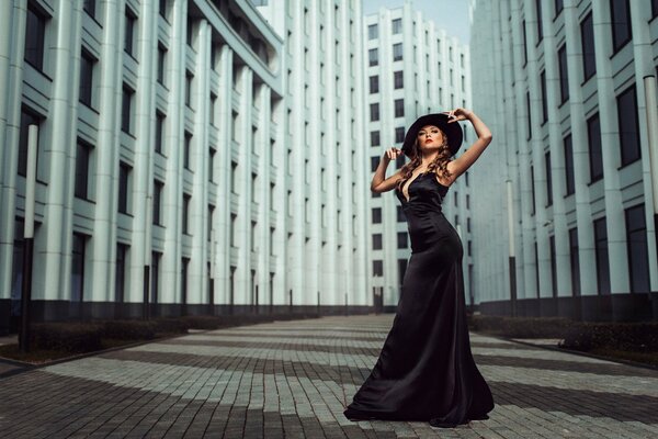 Una chica con una hermosa figura en un vestido negro con escote y sombrero en el fondo de la ciudad