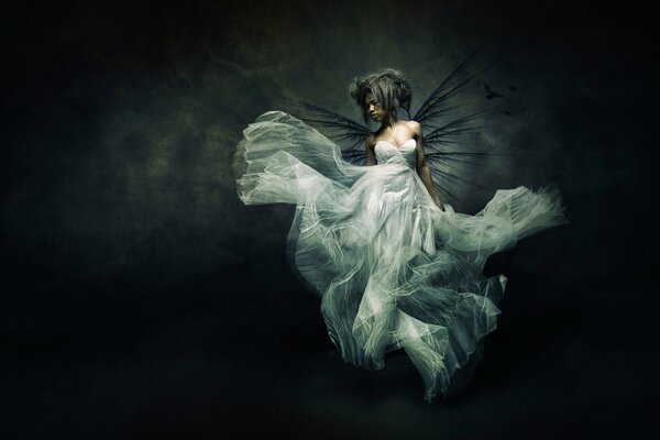 A girl with ragged wings in a bride s dress on a black background