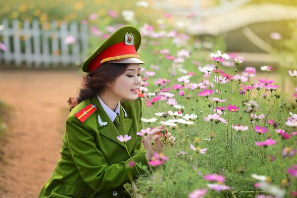 Una ragazza in uniforme militare si siede vicino a un campo di fiori