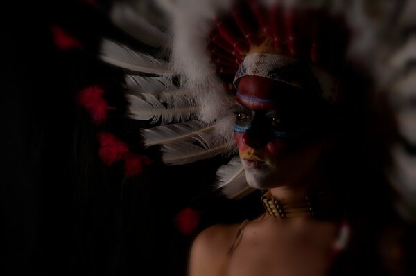 Una chica en medio perfil, pintada al estilo de los indios con un tocado de plumas en la cabeza