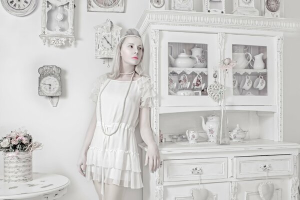 Bambola di porcellana ragazza su sfondo di oggetti bianchi e orologi
