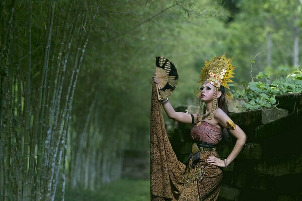 Beautiful girl with a fan on a background of green trees