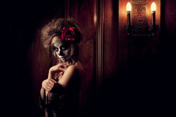 A girl with a face painted for the Day of the dead. The image is complemented by a red flower in the hair