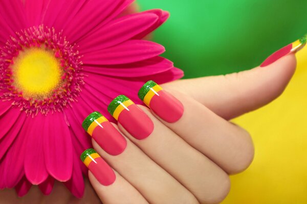 Różowy manicure z kolorowymi paskami na tle gerbera