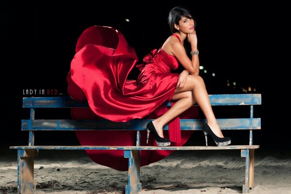 Девушка в красном шелковом платье на скамейке