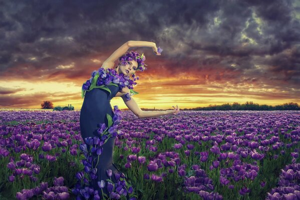 A girl stands in a field with flowers at sunset