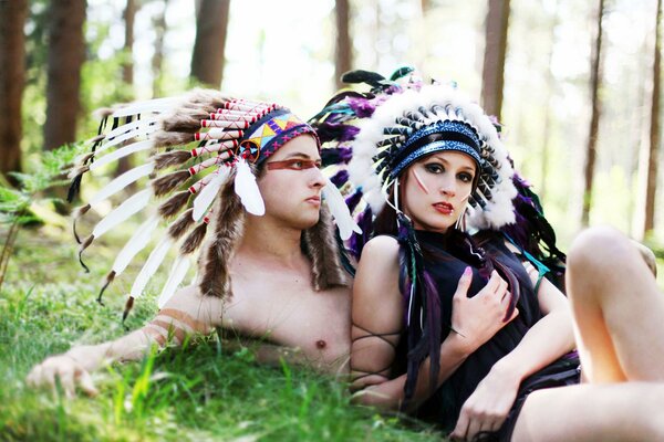 A girl and a guy in feathers are resting in the forest