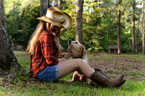 A girl in a hat strokes a dog under a tree