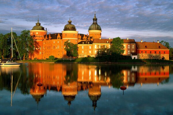 Beautiful red castle reflected in the water with a small yacht