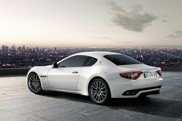 A white maserati stands against the background of the evening city