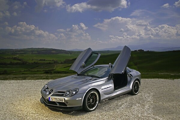 Mercedes with doors opening upwards, against the background of mountains and clouds