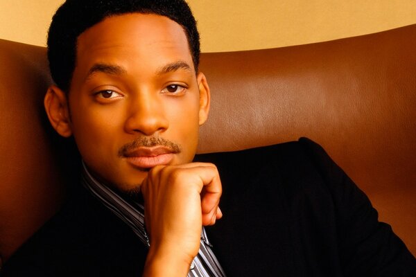 Will Smith in a suit watching on a brown armchair